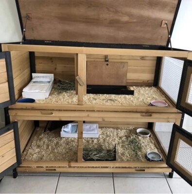 A two storey wooden guinea pig hutch with the doors and roof open to view inside.